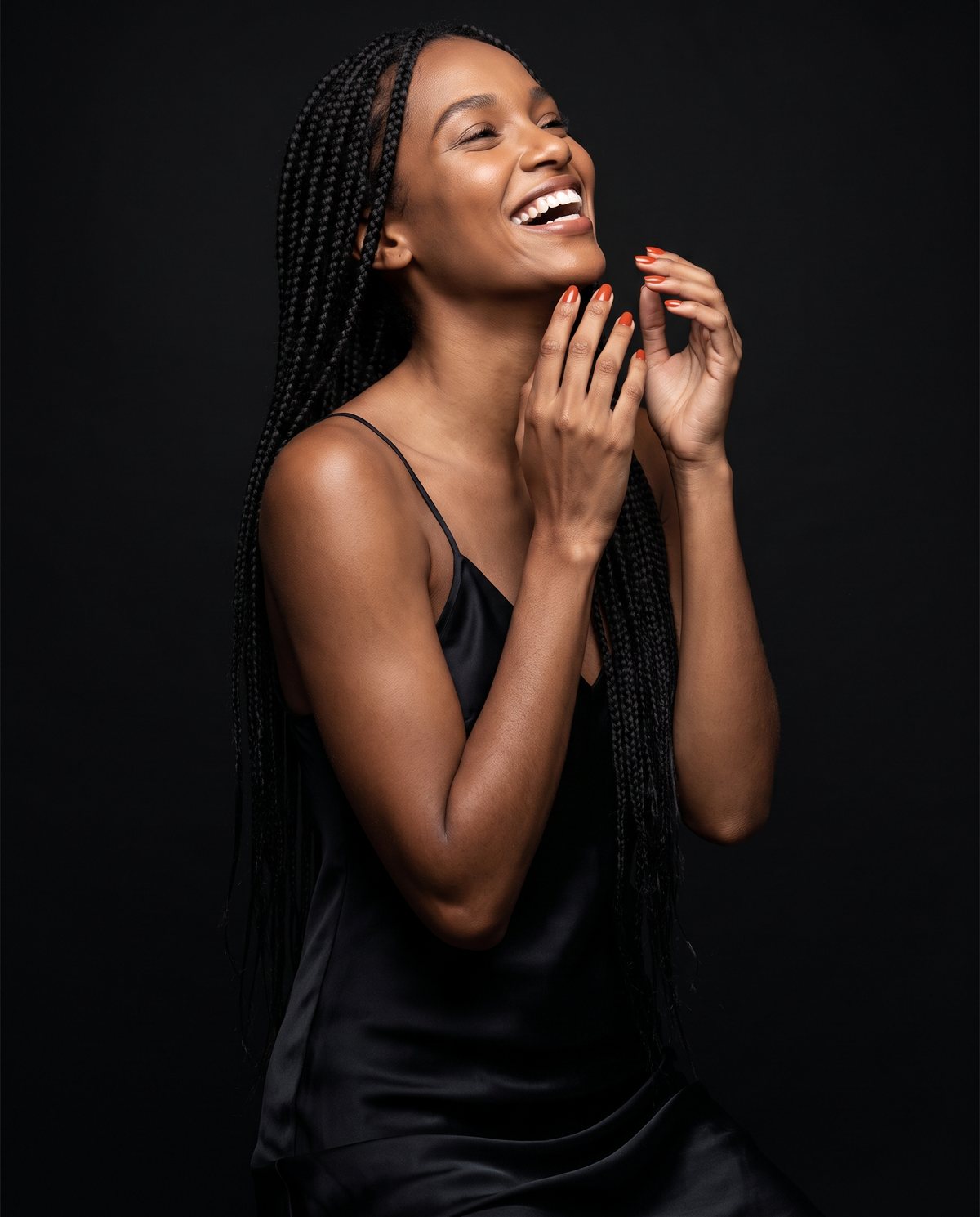 Mulher de tranças sorrindo, com unhas em laranja